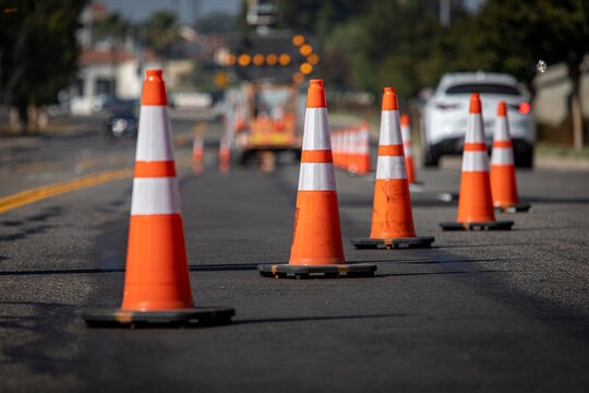Row of high-visibility orange traffic cones with reflective stripes lined up on fresh asphalt road during construction